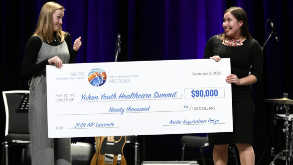 Two young women hold a large cheque for