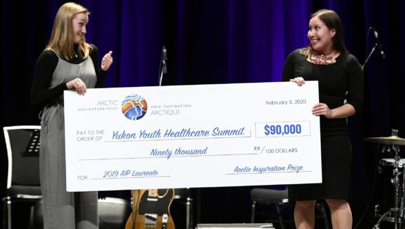 Two young women hold a large cheque for ninety thousand dollars. Deux jeunes femmes tiennent un chèque pour quatre-vingt dix milles dollars.