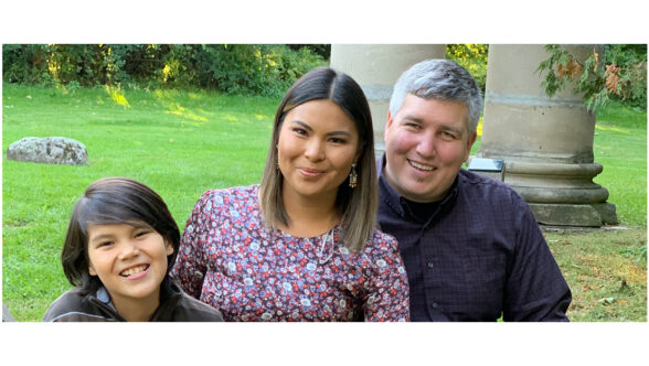 A man, a woman and their child sitting outside, smiling