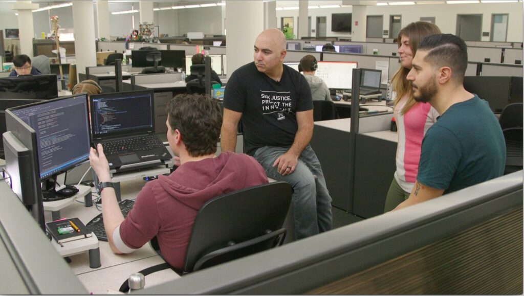 4 people working in office looking at computers in cubicle