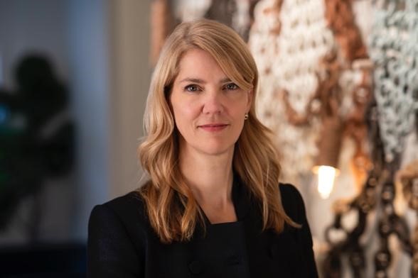 A head and shoulders shot of a woman with long blond hair in a black suit.